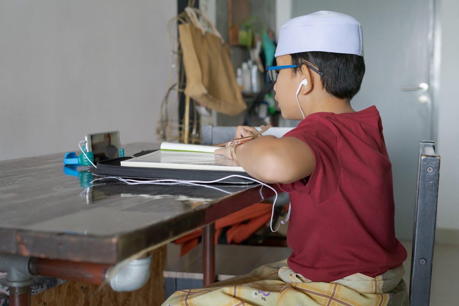 Asian kid reading Al-Quran through video call using smartphone during education and learning from ho